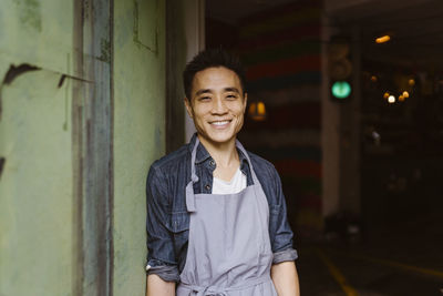 Portrait of smiling restaurant owner in apron leaning on wall