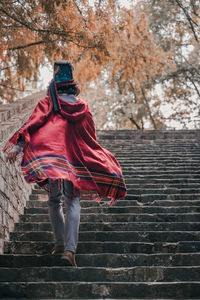 Rear view of man with red cape and top hat against brick wall walking up stairs
