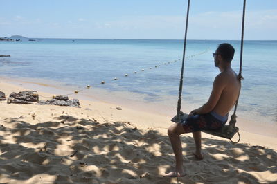 Rear view of woman sitting on shore at beach against sky