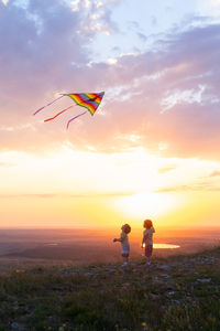 Two happy little kids boys having fun with kite in nature at sunset