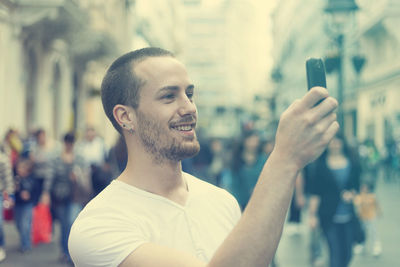Portrait of smiling woman photographing through smart phone in city