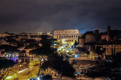 Illuminated city against cloudy sky at night