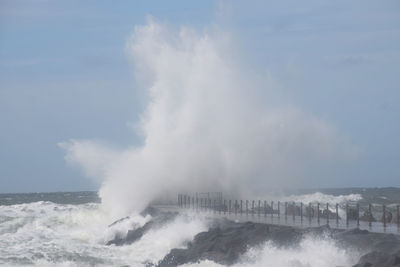 View of waves breaking against cloudy sky