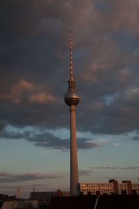 Communications tower in city against sky during sunset