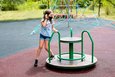 Girl wearing mask playing on carousel at playground