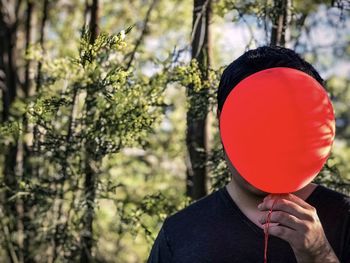 Midsection of person holding red balloon against trees.