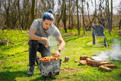 Young man preparing barbecue skewers in the forest during springtime