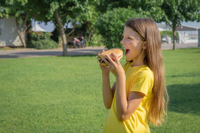 Happy teenage girl eating a burger in the park outdoors.