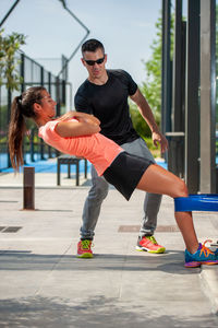 Man helping woman exercising on footpath in city