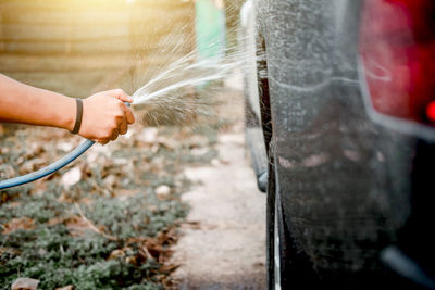 Cropped hand pouring water on car through pipe