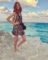 Portrait of smiling young woman standing on beach against sky