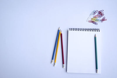 Directly above shot of colorful pencils and note pad on white background