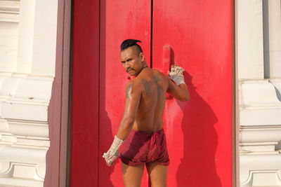 Full length of shirtless man standing against door