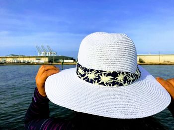 Rear view of woman holding hat against sea