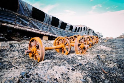 Abandoned train by wheels on field against sky
