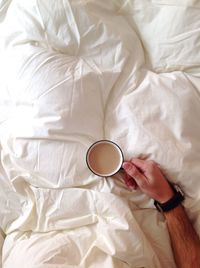 Directly above shot of woman holding coffee cup on bed at home