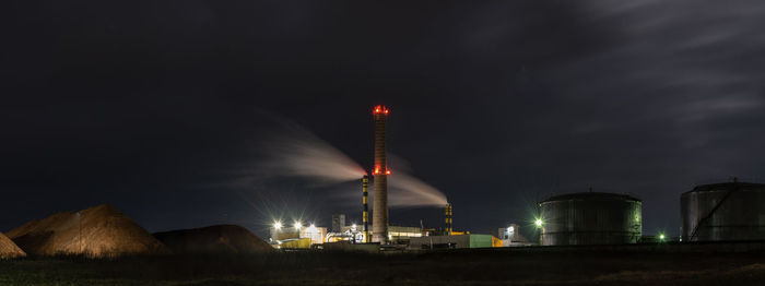 Low angle view of illuminated factory against sky at night