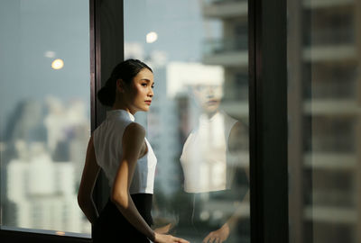 Businesswoman looking away while standing by window at office