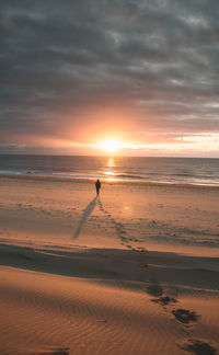 Silhouette man standing on beach against sky during sunset