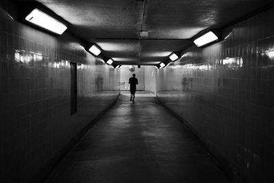 Rear view of person walking in illuminated tunnel