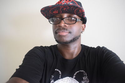 Man wearing cap and eyeglasses against wall