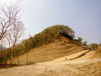 Dirt road amidst trees against clear sky