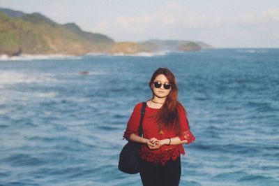 Portrait of young woman wearing sunglasses standing at beach