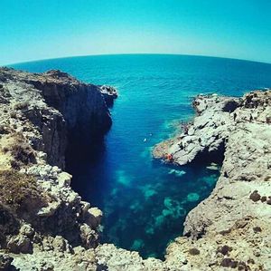 Rock formations by sea against clear blue sky