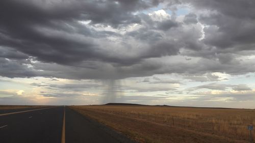 Road passing through field against cloudy sky