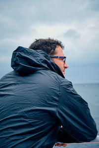 Rear view of man looking away while standing by railing against sky