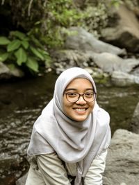 Portrait of smiling young woman sitting on rocks by stream