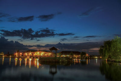 Illuminated buildings by lake against sky at night