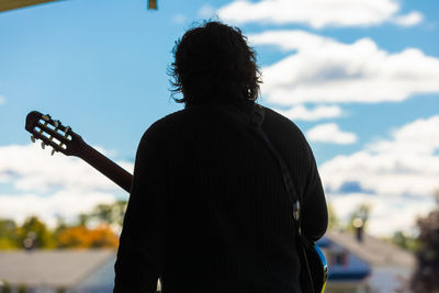 Rear view of man playing guitar against sky