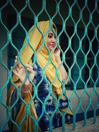 Young woman in hijab talking on mobile phone seen through metal grate