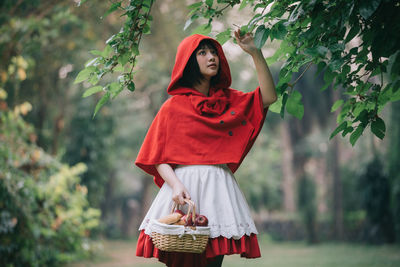 Portrait of woman with red umbrella standing against plants