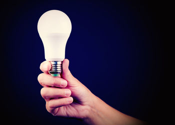 Midsection of woman holding light bulb against black background