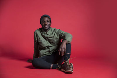 Portrait of young man sitting against red background