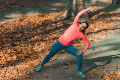 Woman stretching while standing on footpath in park during autumn