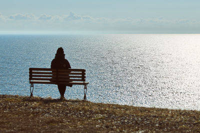 Rear view of woman sitting on beach against sky