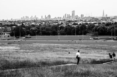 People on field by buildings against sky