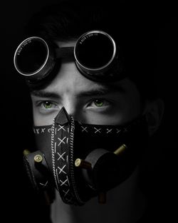 Close-up of young man wearing gas mask standing against black background