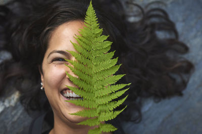 Woman with a fern on her face. she's lying on a rock and covers half her face with a fern leaf.
