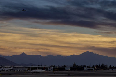 Airplane flying over mountains against sky during sunset