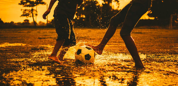 Low section of man playing soccer ball on field during sunset