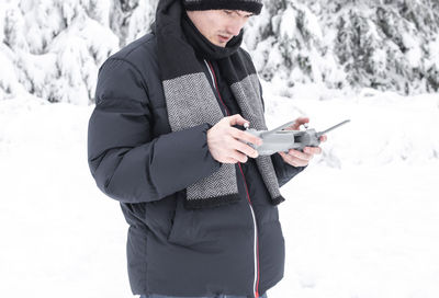 A young man controls a drone through a remote control in a winter forest.