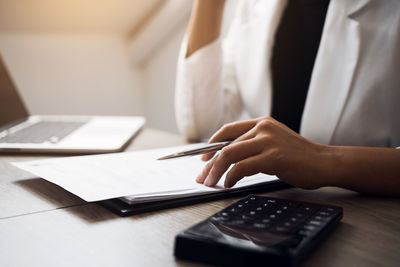 Midsection of businesswoman analyzing paperwork on table