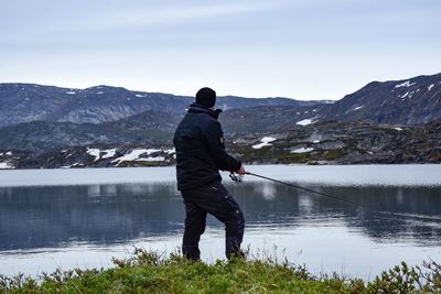 Man fishing in lake against mountains