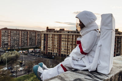 Young female astronaut sitting on retaining wall during sunset