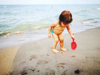Full length of shirtless baby girl playing on shore at beach