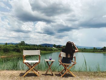 Rear view of woman sitting on chair at beach against sky